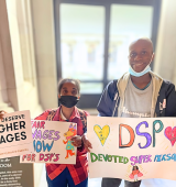 Janelle and Steven stand side-by-side holding signs supporting increasing salary of DSPs