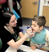 Julia Gonzalez, SLP, is holding something to Lukas's mouth for feeding therapy