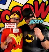 Janice, dressed as Wonder Woman, and her boyfriend, dressed as Batman, post in front of a comicbook background