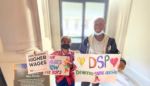 Janelle and Steven stand side-by-side holding signs supporting increasing salary of DSPs