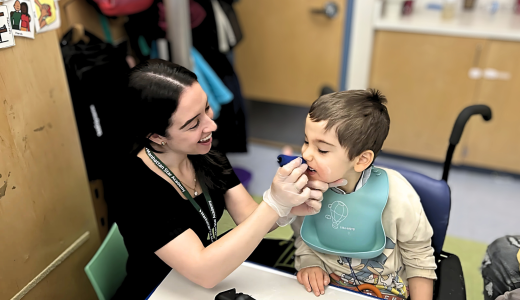 Julia Gonzalez, SLP, is holding something to Lukas's mouth for feeding therapy