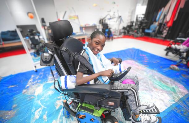young student in his powerchair in the middle of some powerchair art on the ground. He looks very proud.