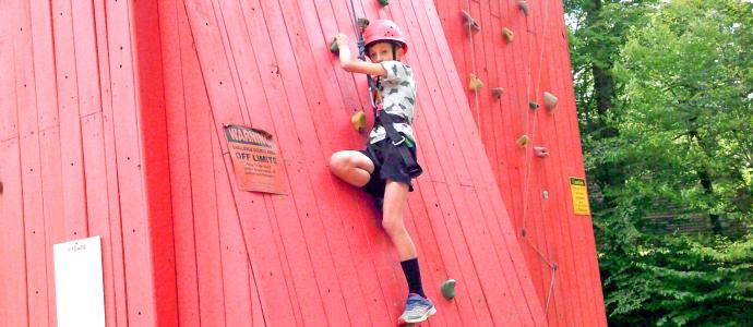 Child wearing rock climbing harness appears to be ascending on a red climbing wall.