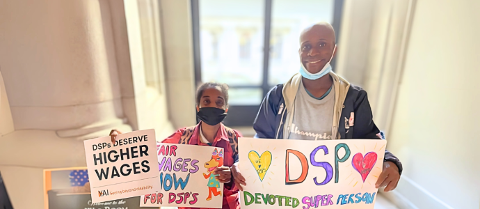 Janelle and Steven stand side-by-side holding signs supporting increasing salary of DSPs