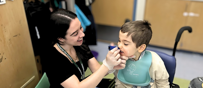 Julia Gonzalez, SLP, is holding something to Lukas's mouth for feeding therapy