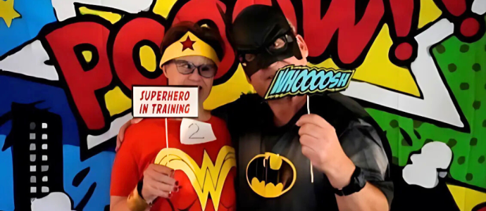 Janice, dressed as Wonder Woman, and her boyfriend, dressed as Batman, post in front of a comicbook background