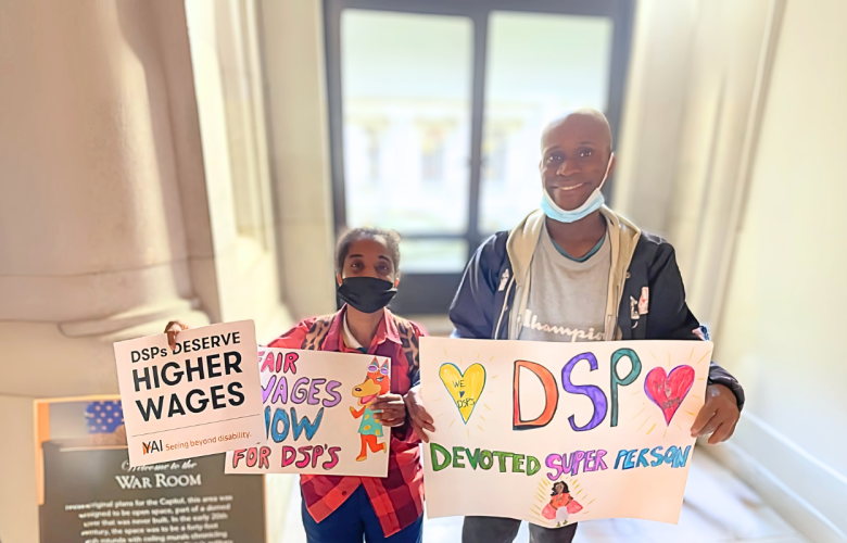 Janelle and Steven stand side-by-side holding signs supporting increasing salary of DSPs