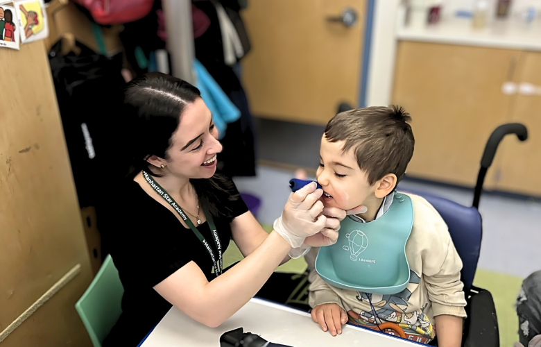 Julia Gonzalez, SLP, is holding something to Lukas's mouth for feeding therapy