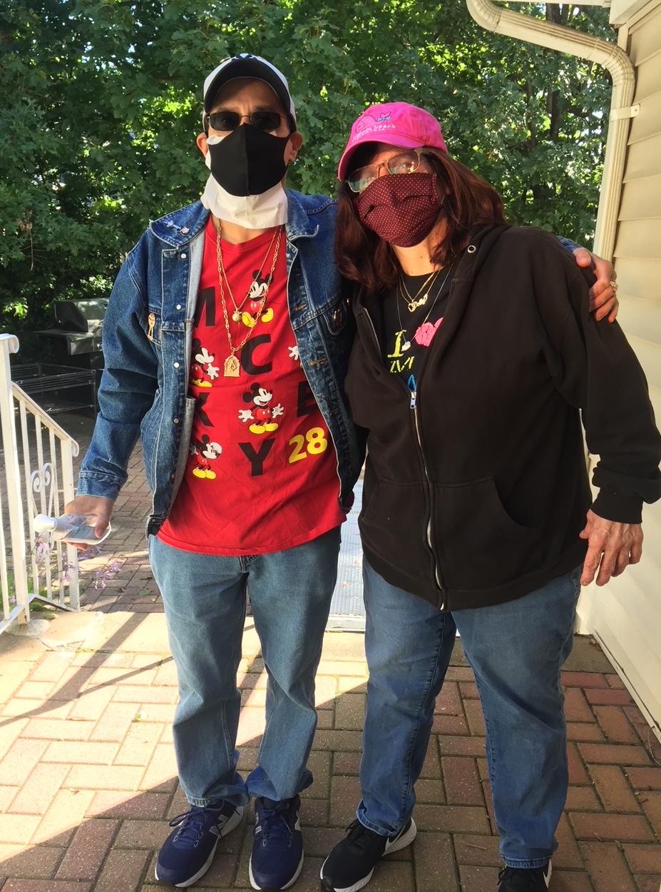 Chris and Dorothy stand outside together, they are looking at the camera and wearing facemasks