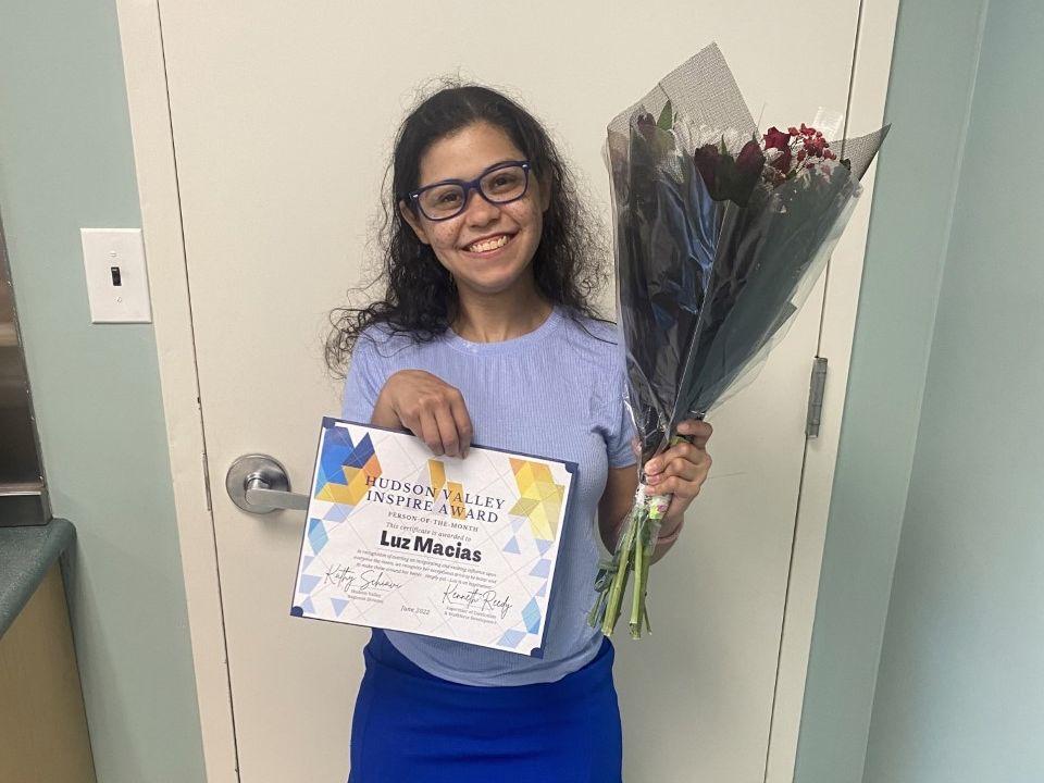 Person wearing glasses and purple clothes holds a certificate and a bunch of flowers