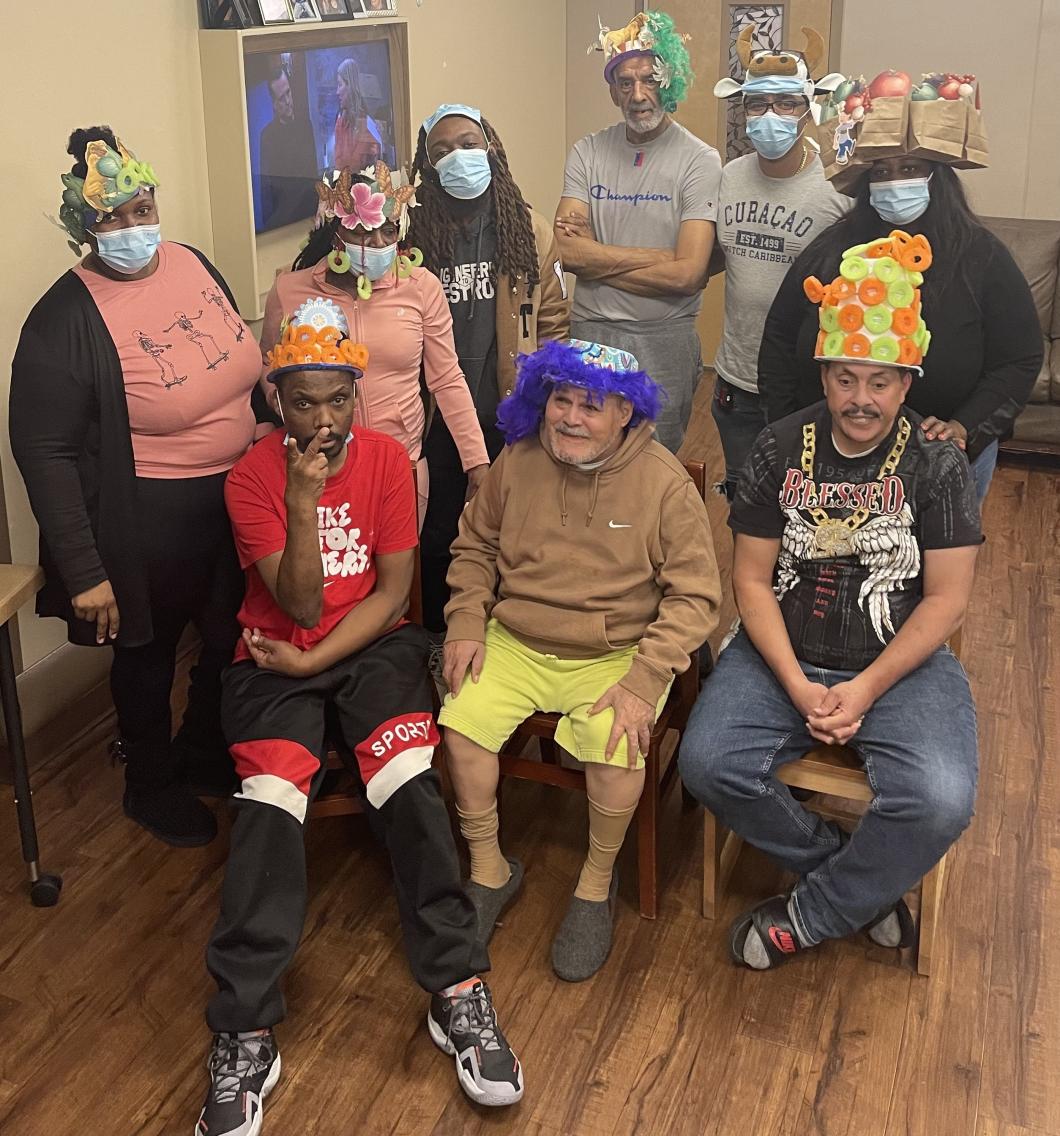 Group of people, standing and sitting, pose for photo in colorful handmade hats.