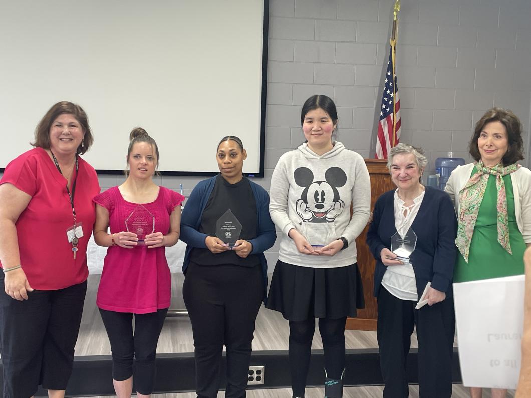 Group of 6 people stand in a row, 4 in the middle hold awards