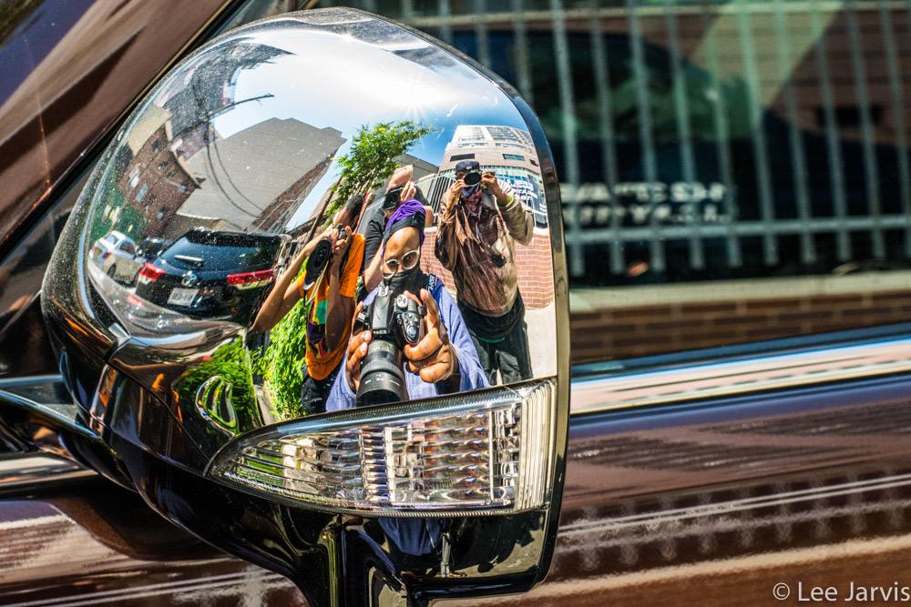 Photo of reflective chrome car wing mirror, you can see multiple people with cameras in the reflection