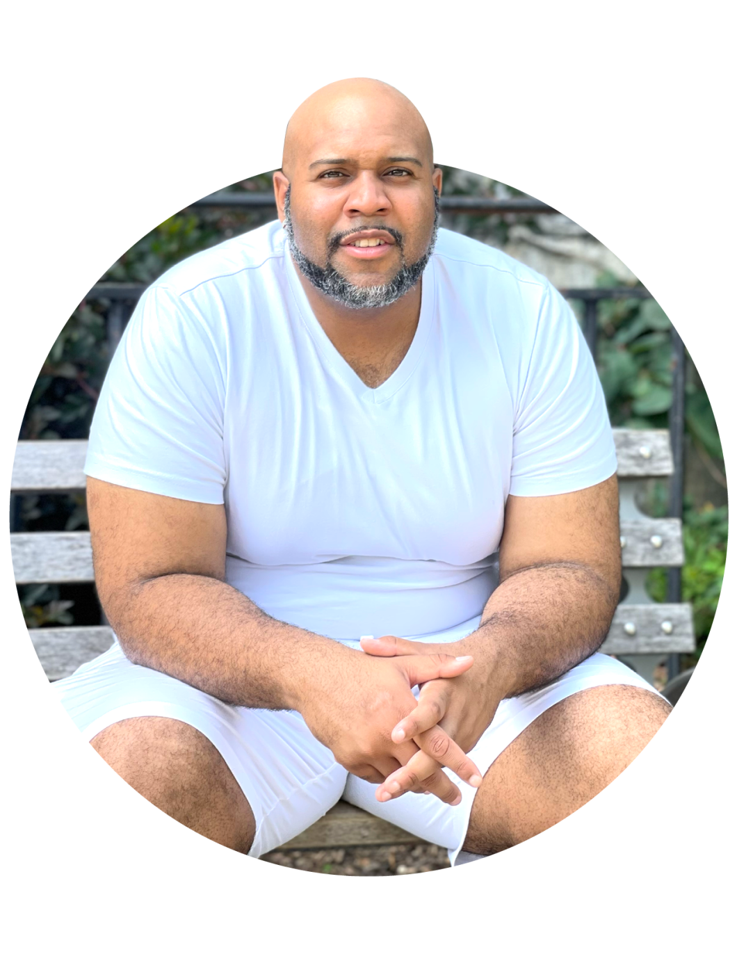 Angelo wears all white as he sits on a bench and looks at the camera