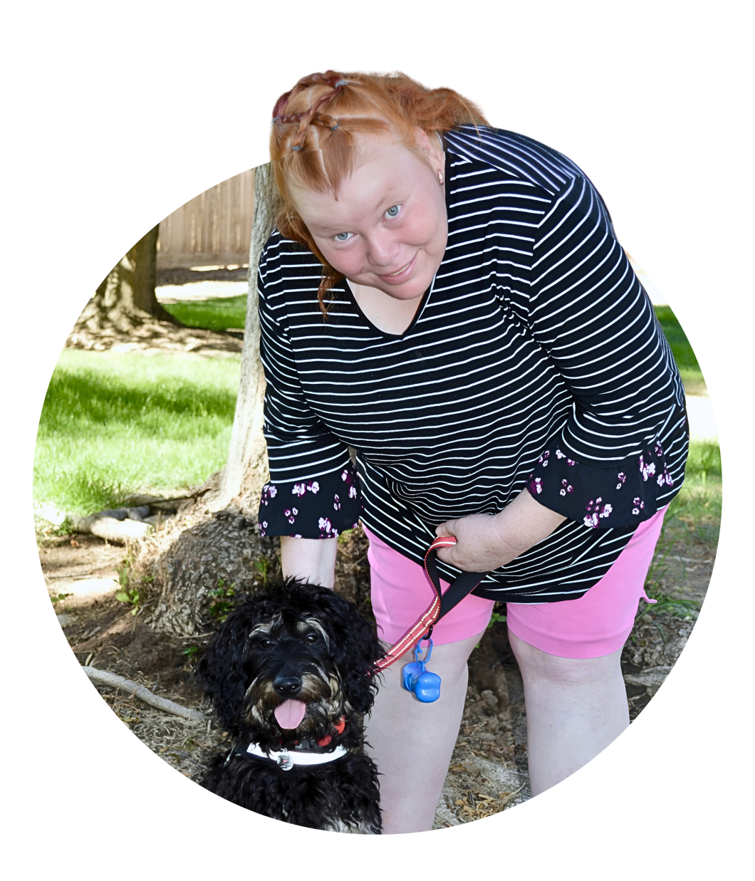 woman with red hair leans over a dog while looking up at the camera for photo