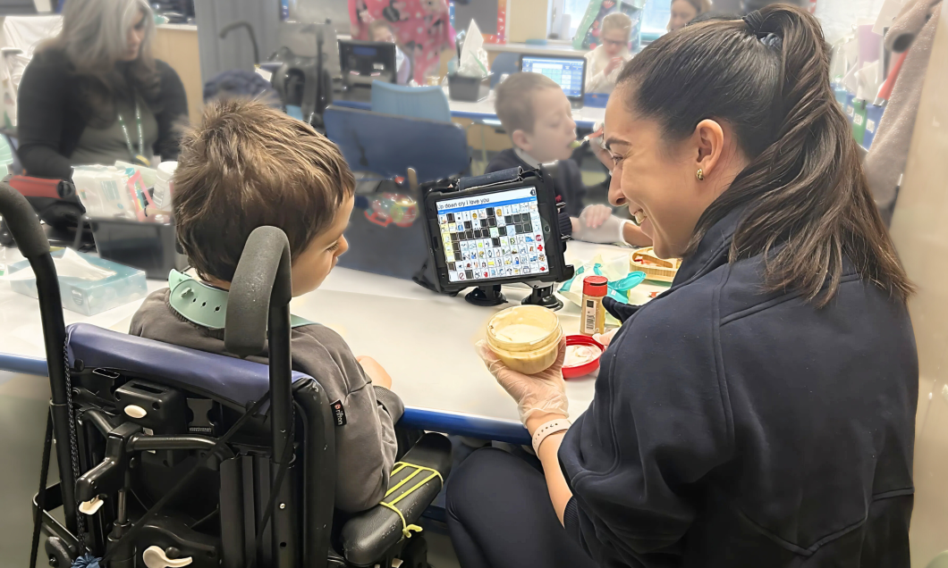 Julia Gonzalez sits with Lukas to give feeding therapy, she's holding a container with a paste-like substance.