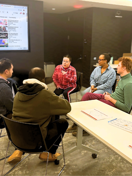 Amanda sits in a group circle with 4 other people, sharing her experiences